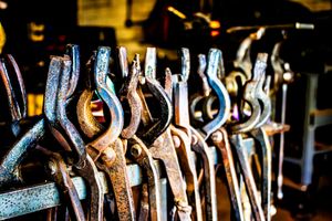 Row of rusty vintage metal clamps and tools hanging in a workshop, showcasing aged industrial equipment.