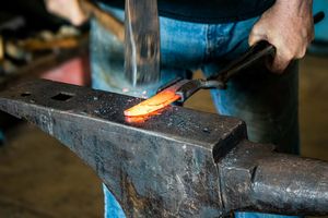 Blacksmith hammering glowing red-hot metal on an anvil in a professional forge workshop.