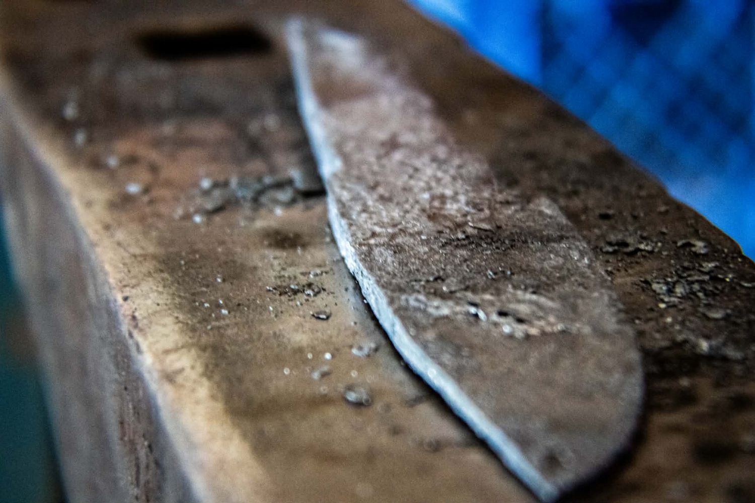 Close-up of a rusty metal blade resting on a worn wooden surface with water droplets visible.