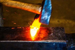A glowing red-hot metal blade being forged on an anvil with a hammer, sparks flying in a blacksmith workshop.