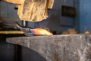 Red-hot metal piece resting on a blacksmith anvil during forging process in a traditional smithy workshop.