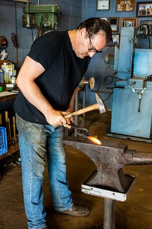 Blacksmith forging glowing hot metal on an anvil with a hammer in a traditional workshop.