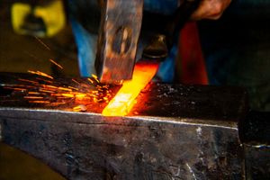 Close-up of a blacksmith striking heated metal on an anvil with bright sparks flying.