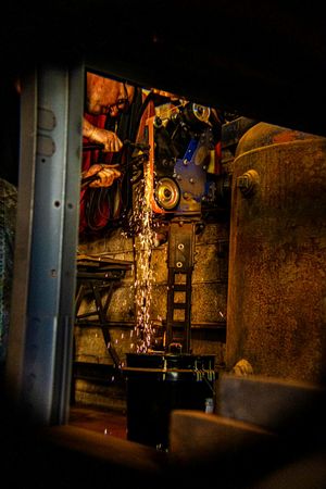 Worker grinding metal with angle grinder creating bright sparks in dark industrial workshop.