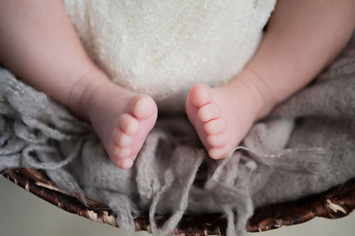 Wedding rings resting on newborn baby toes with blurred infant in soft focus background.