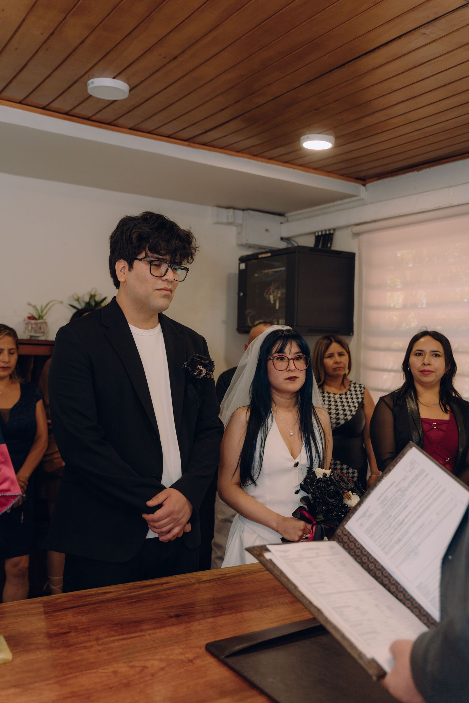 Couple stands at altar during civil wedding ceremony with guests watching in background.