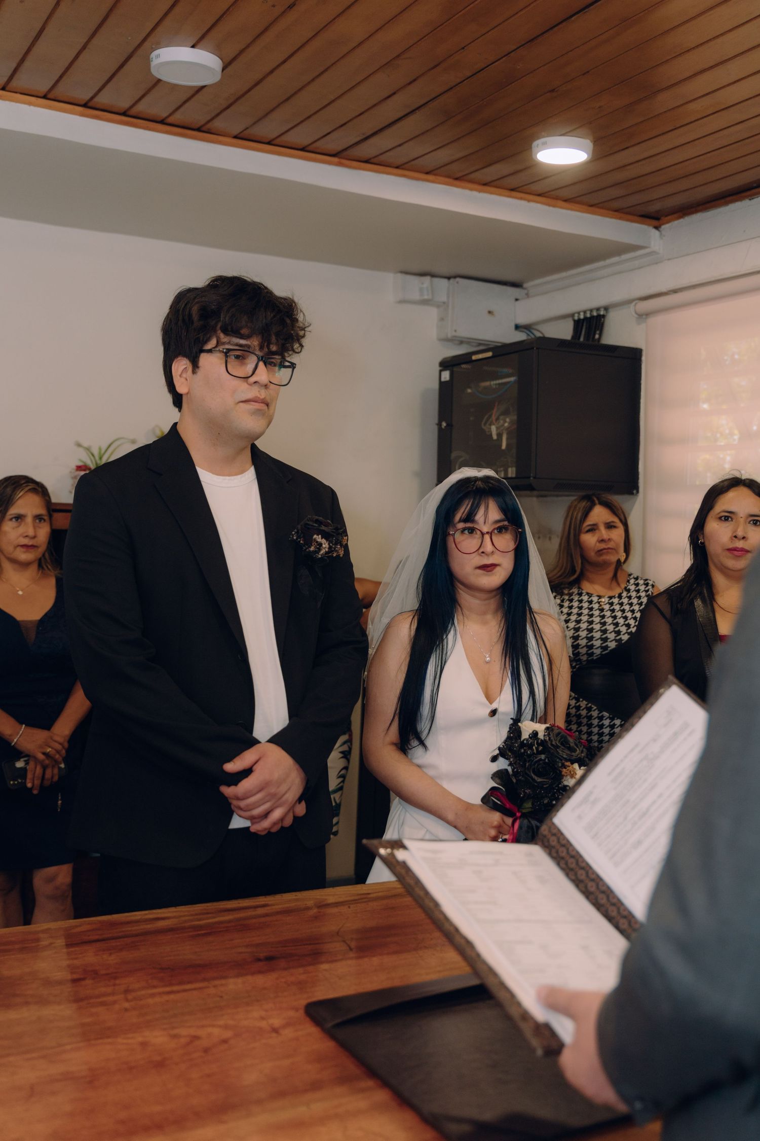 Bride and groom stand solemnly before officiant reading from registry during wedding ceremony.