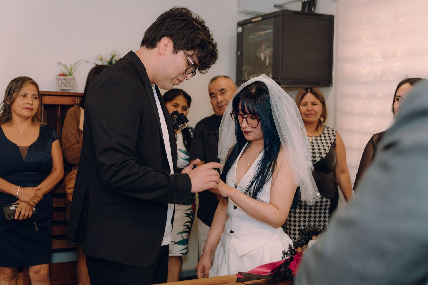 Groom placing wedding ring on brides finger during civil ceremony with guests watching.