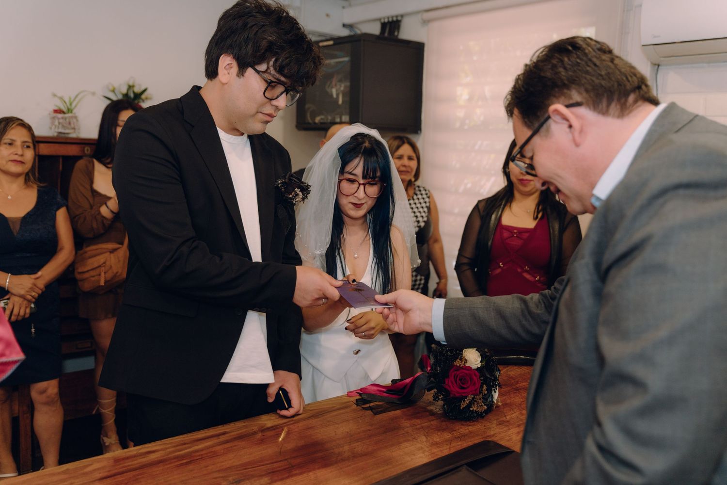 Couple receiving wedding rings from officiant during civil ceremony at wooden table.