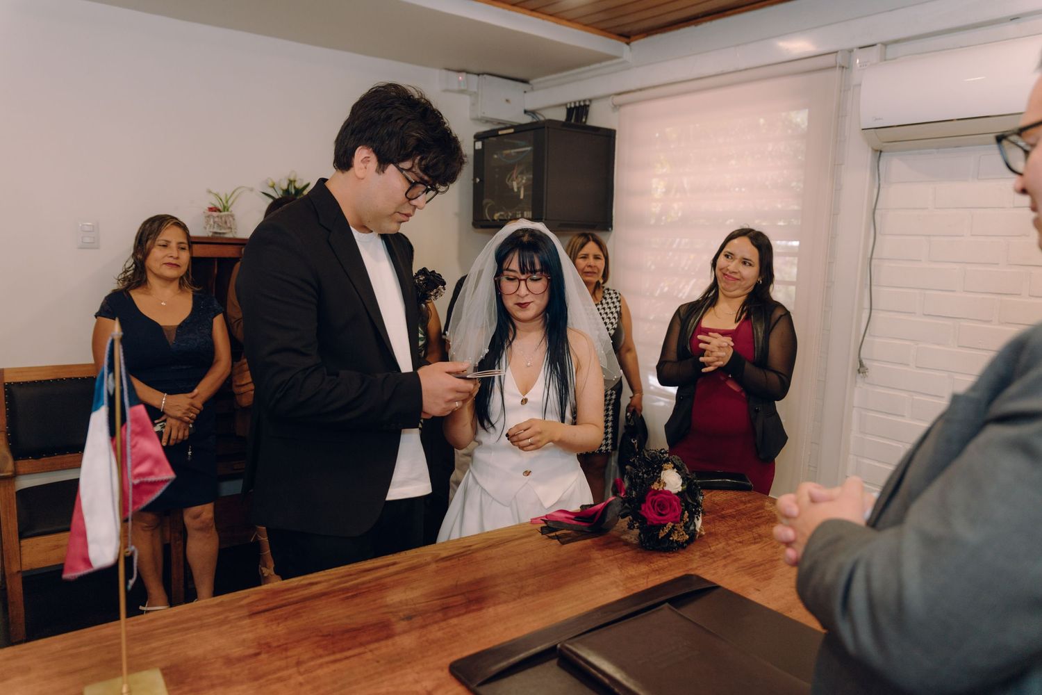 Groom placing wedding ring on brides finger at civil ceremony with guests watching.