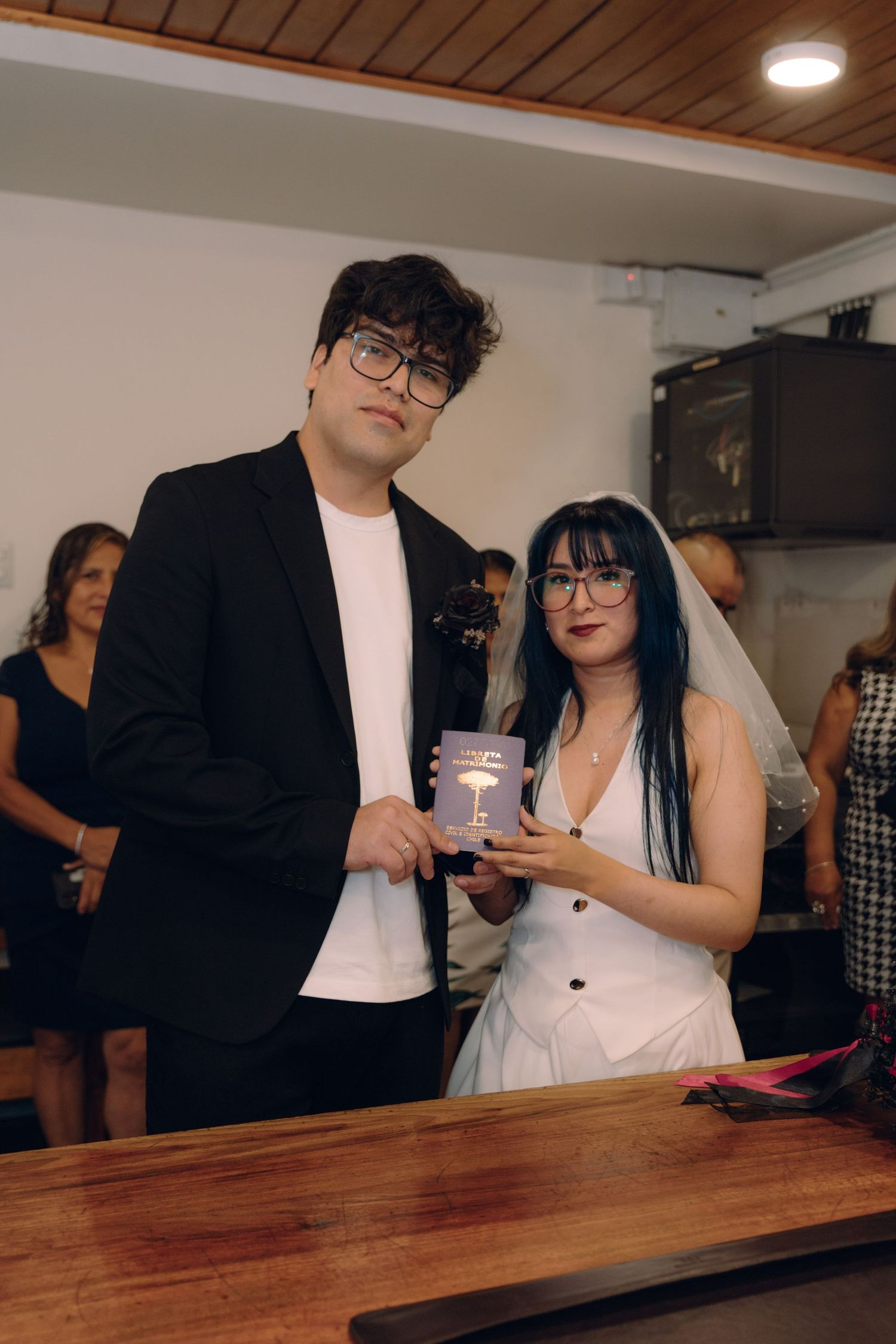Newlywed couple poses holding marriage certificate at civil wedding ceremony, bride in white dress and veil.