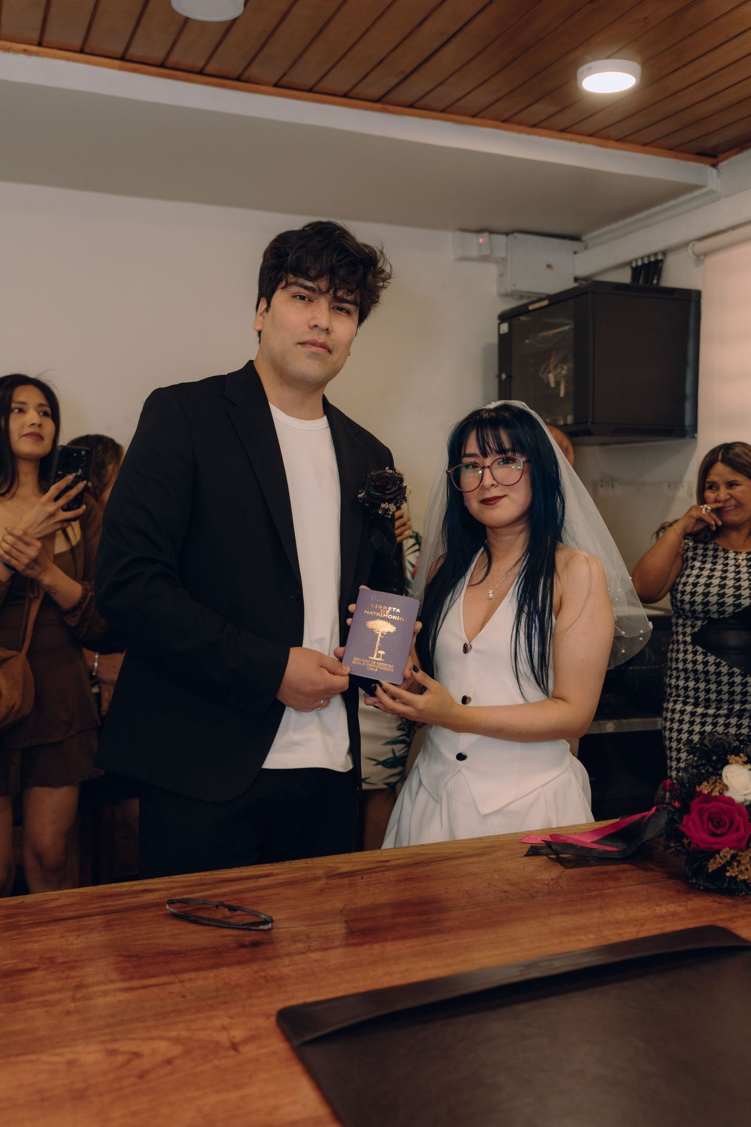 Bride with blue hair and groom in black suit display marriage certificate at civil wedding ceremony.