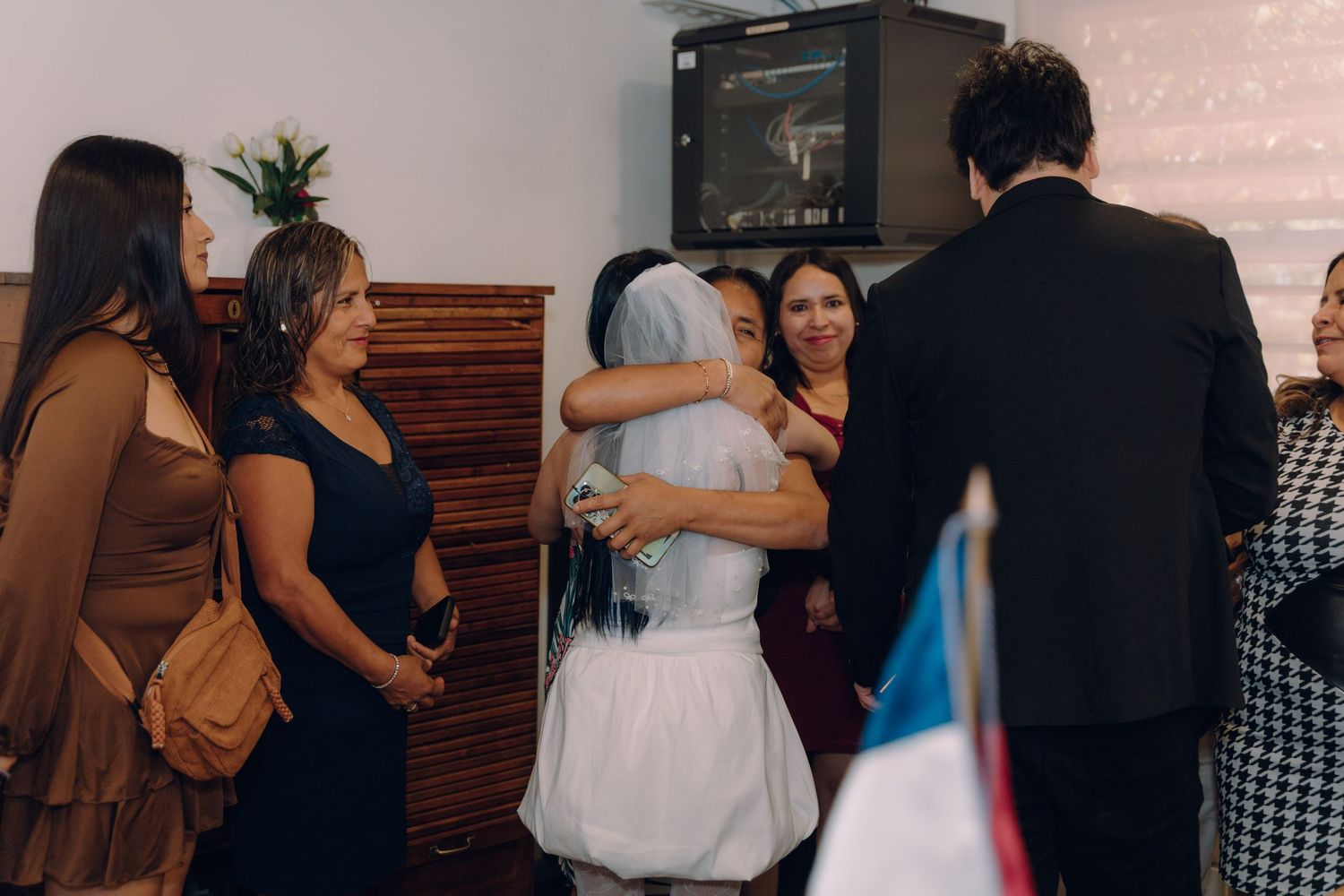 Bride with blue hair hugs wedding guest while family and friends celebrate at intimate ceremony.