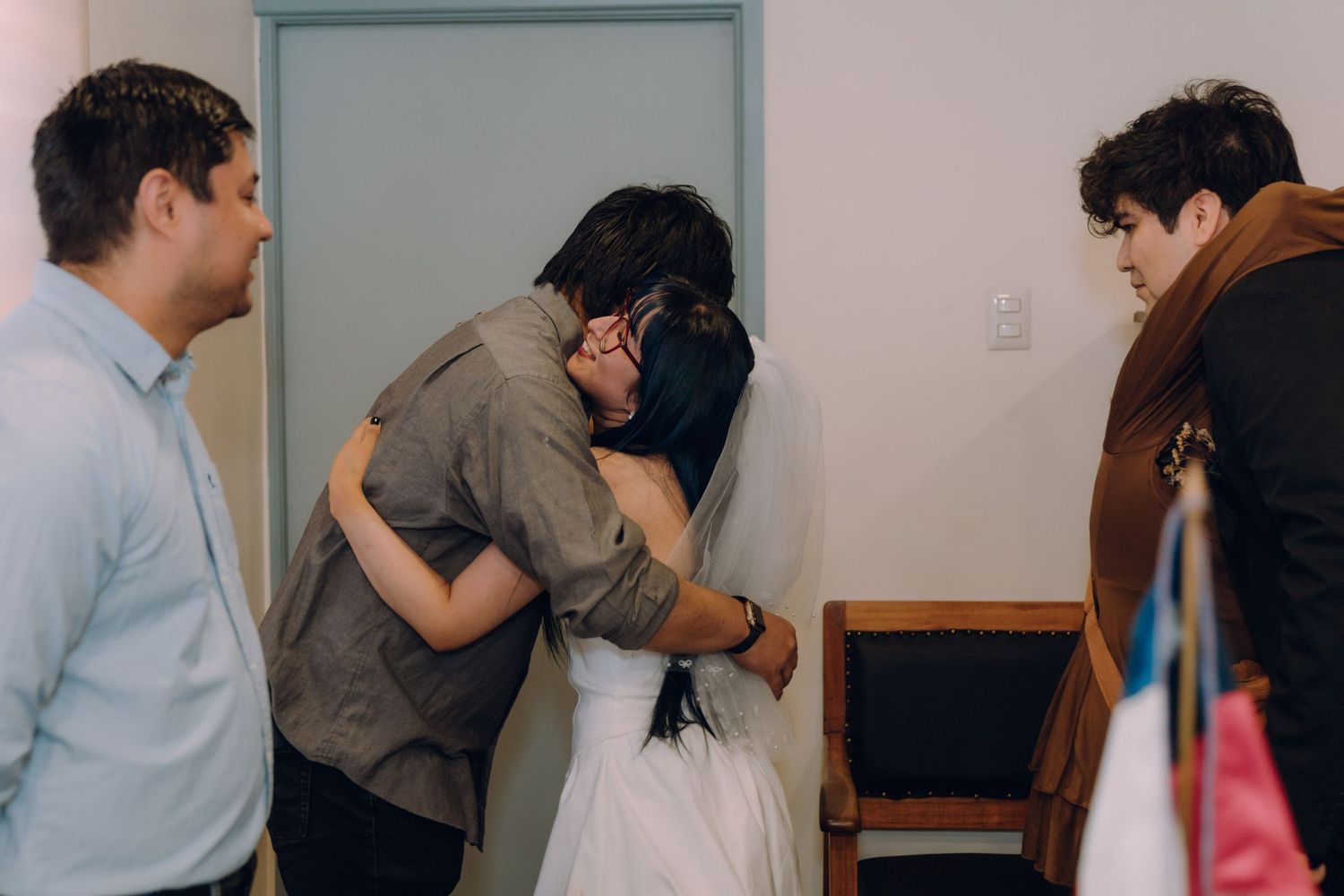 Bride receives emotional hug from family member while guests look on at intimate wedding ceremony.