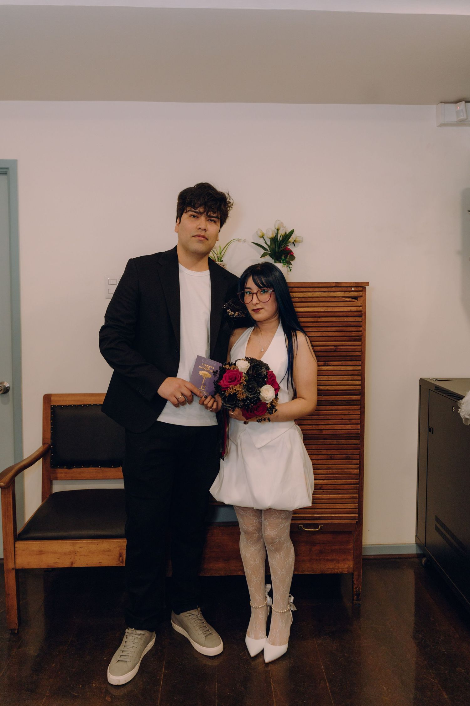 Newlywed couple poses with marriage certificate and bridal bouquet at their intimate civil wedding ceremony.