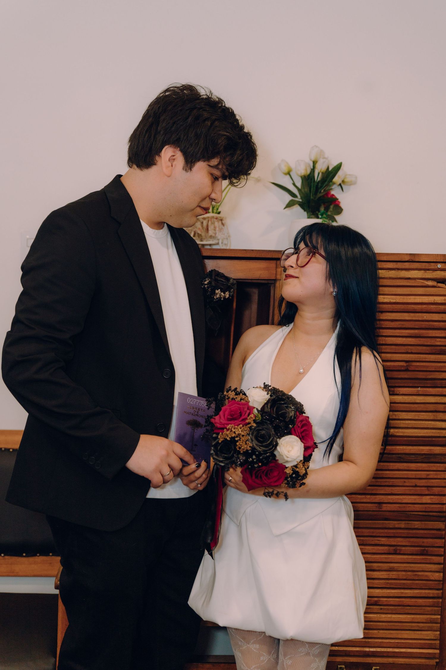 Couple in wedding attire sharing a tender moment, bride in white dress holding red and black bouquet.