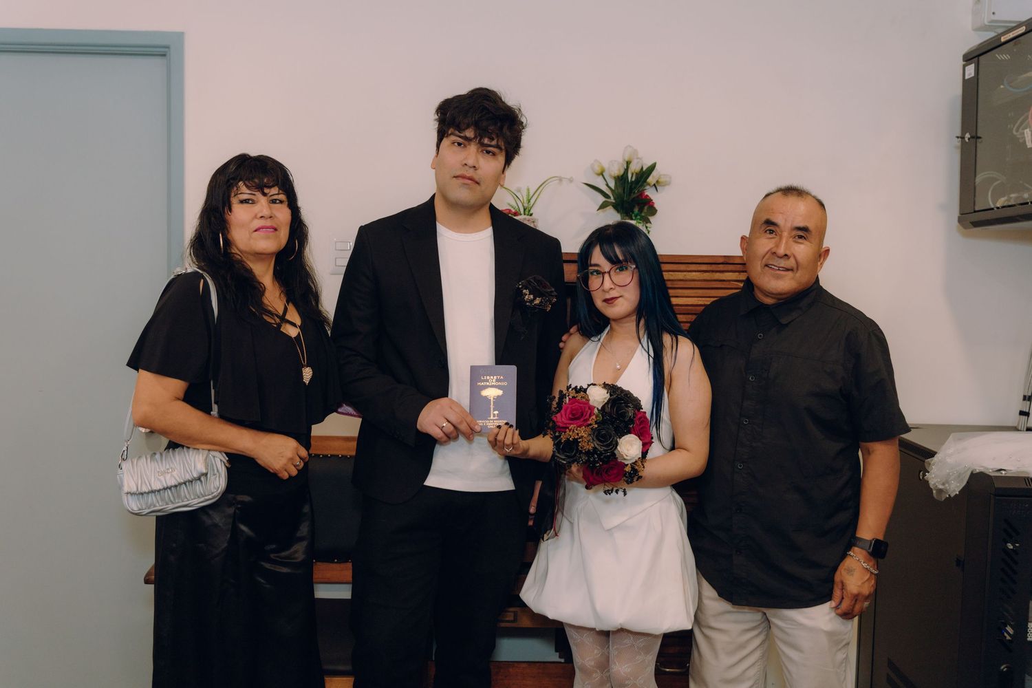 Wedding couple poses with two family members in a simple indoor ceremony setting.