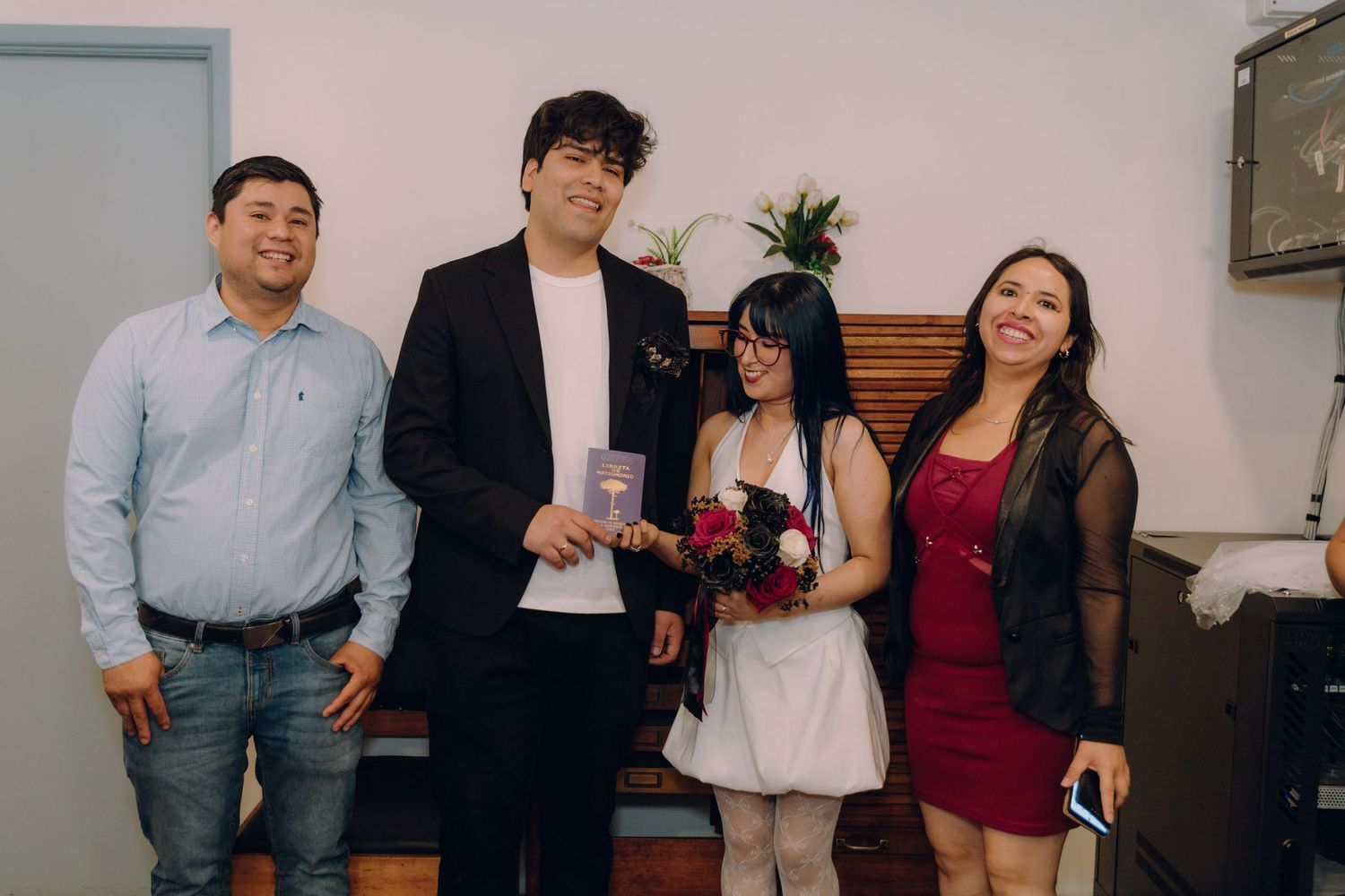 Wedding couple celebrates with two smiling guests in casual indoor ceremony setting.