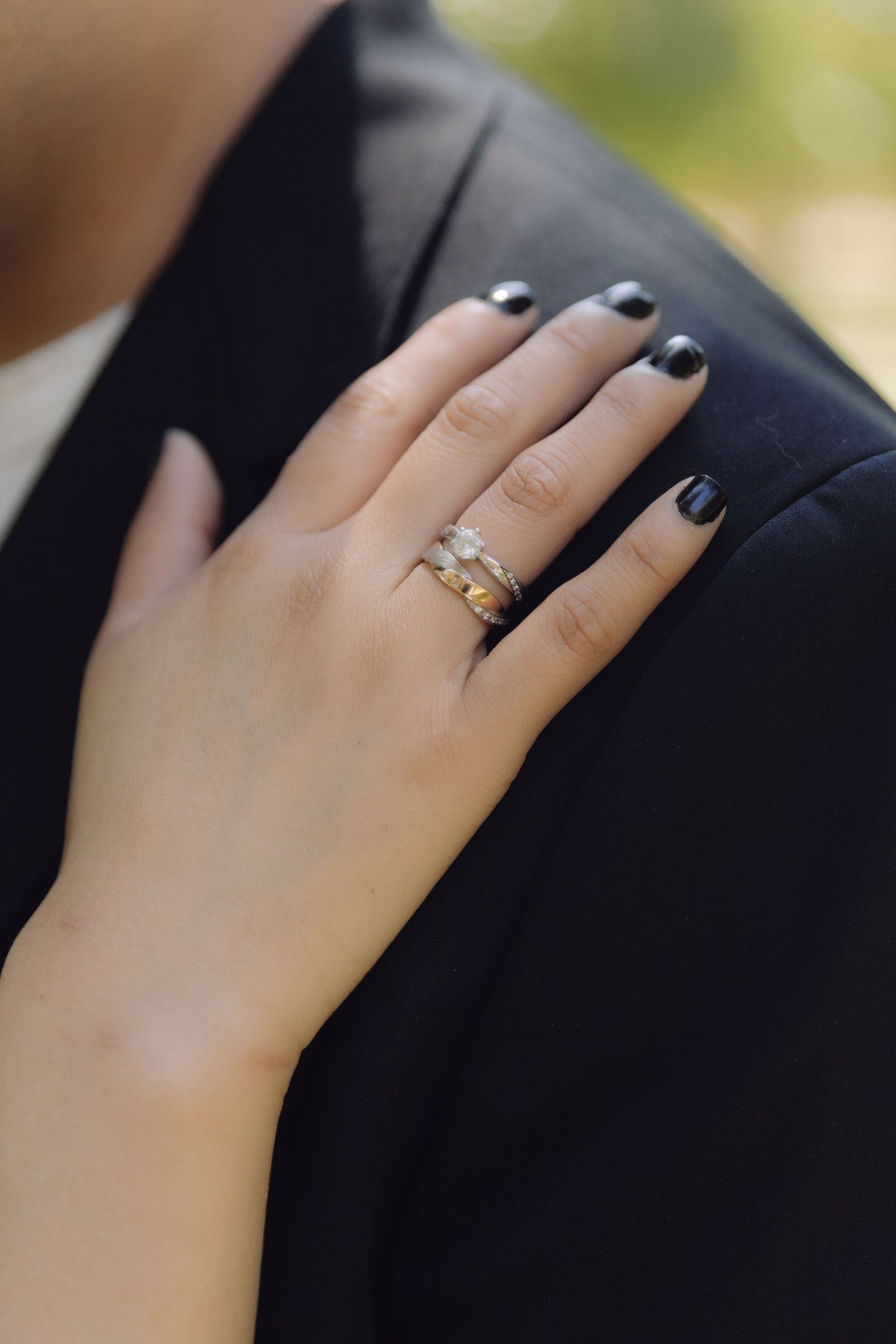 Close-up of bride hand with stacked gold rings and black nail polish resting on grooms dark suit jacket.