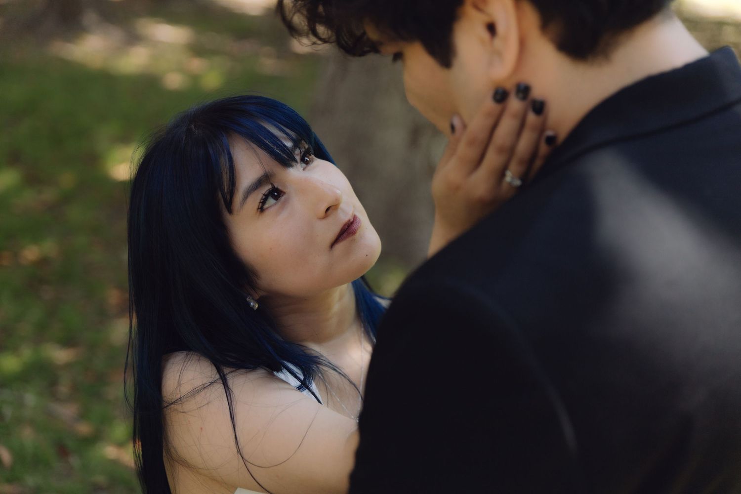 Intimate close-up of bride with blue hair looking up at groom lovingly, hand on his face outdoors.