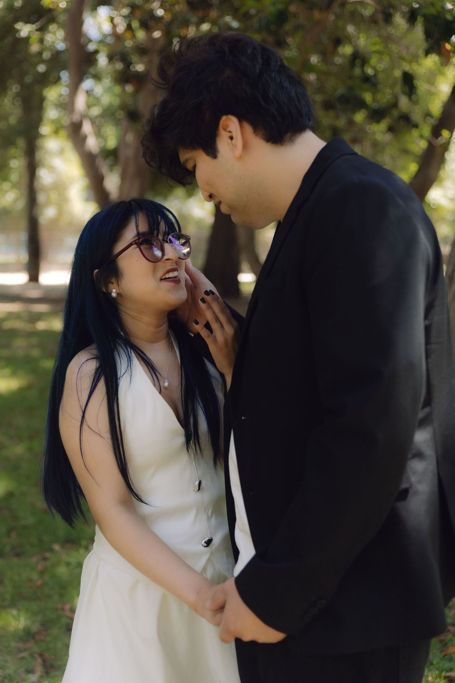 Couple sharing a romantic moment in a park, woman in white dress smiling up at man in black suit.