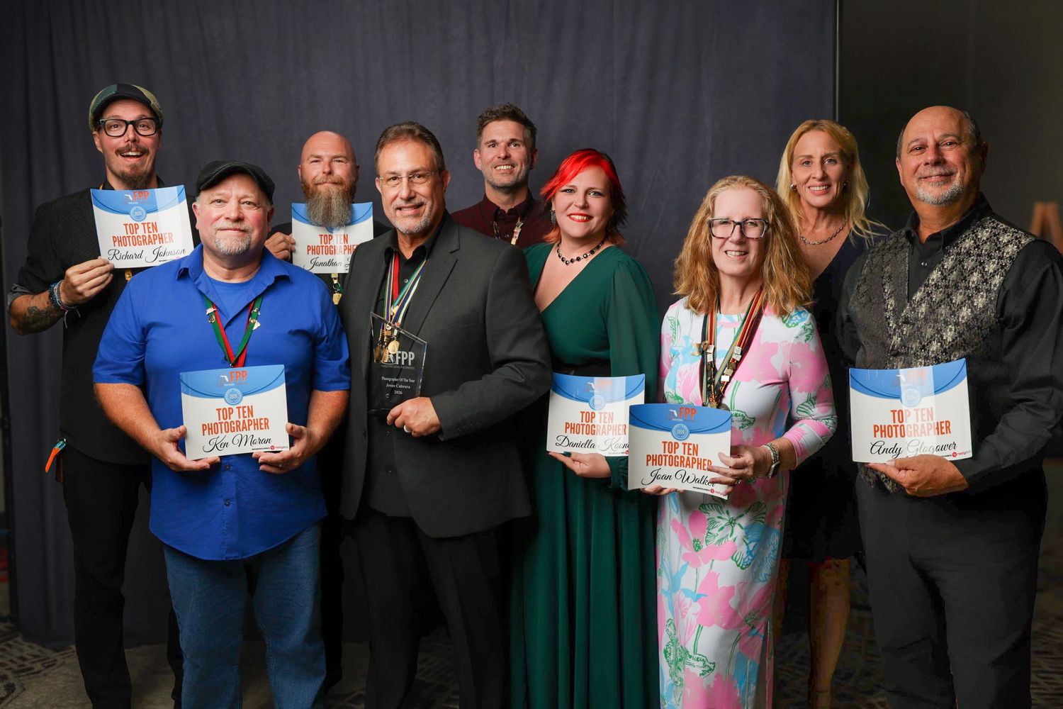 Group of nine people smiling and holding books or programs at an awards ceremony or special event.