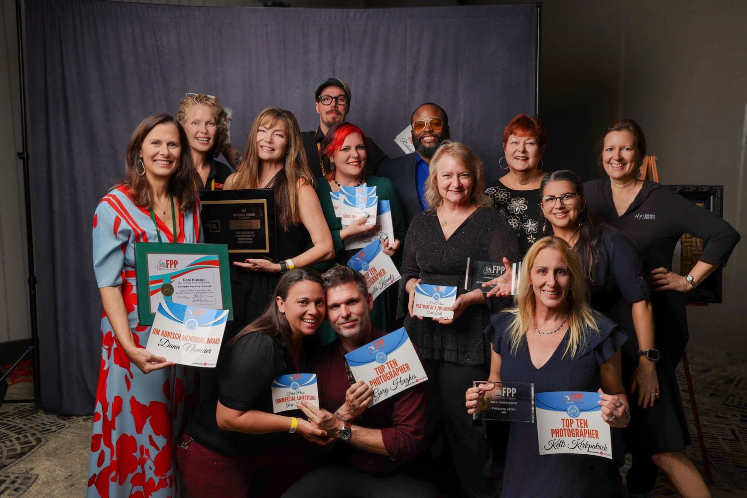 Group of award winners posing together holding plaques and certificates at a formal recognition ceremony.