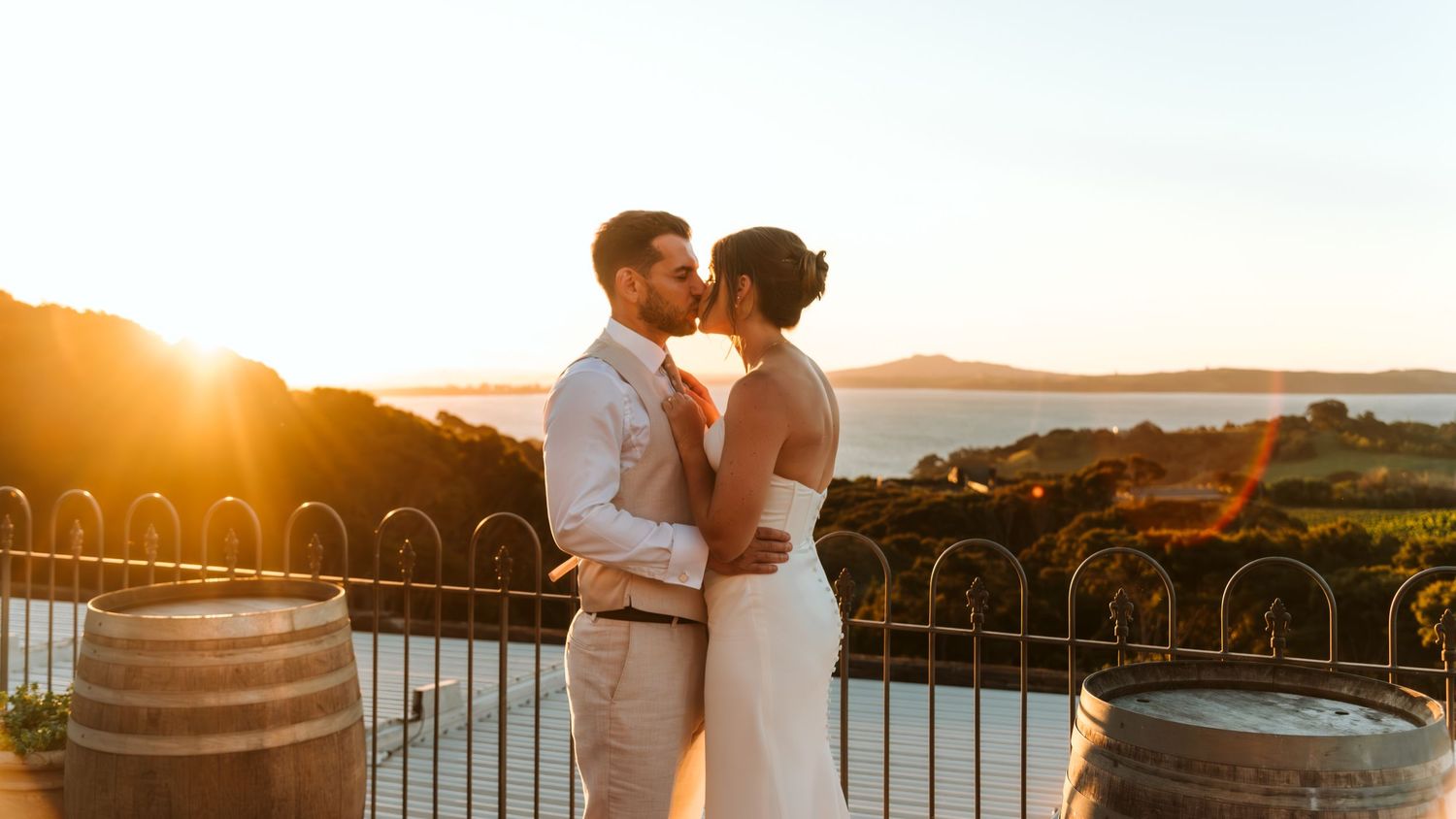 Couple sharing a romantic kiss at sunset on a vineyard terrace with scenic coastal views on their wedding day.