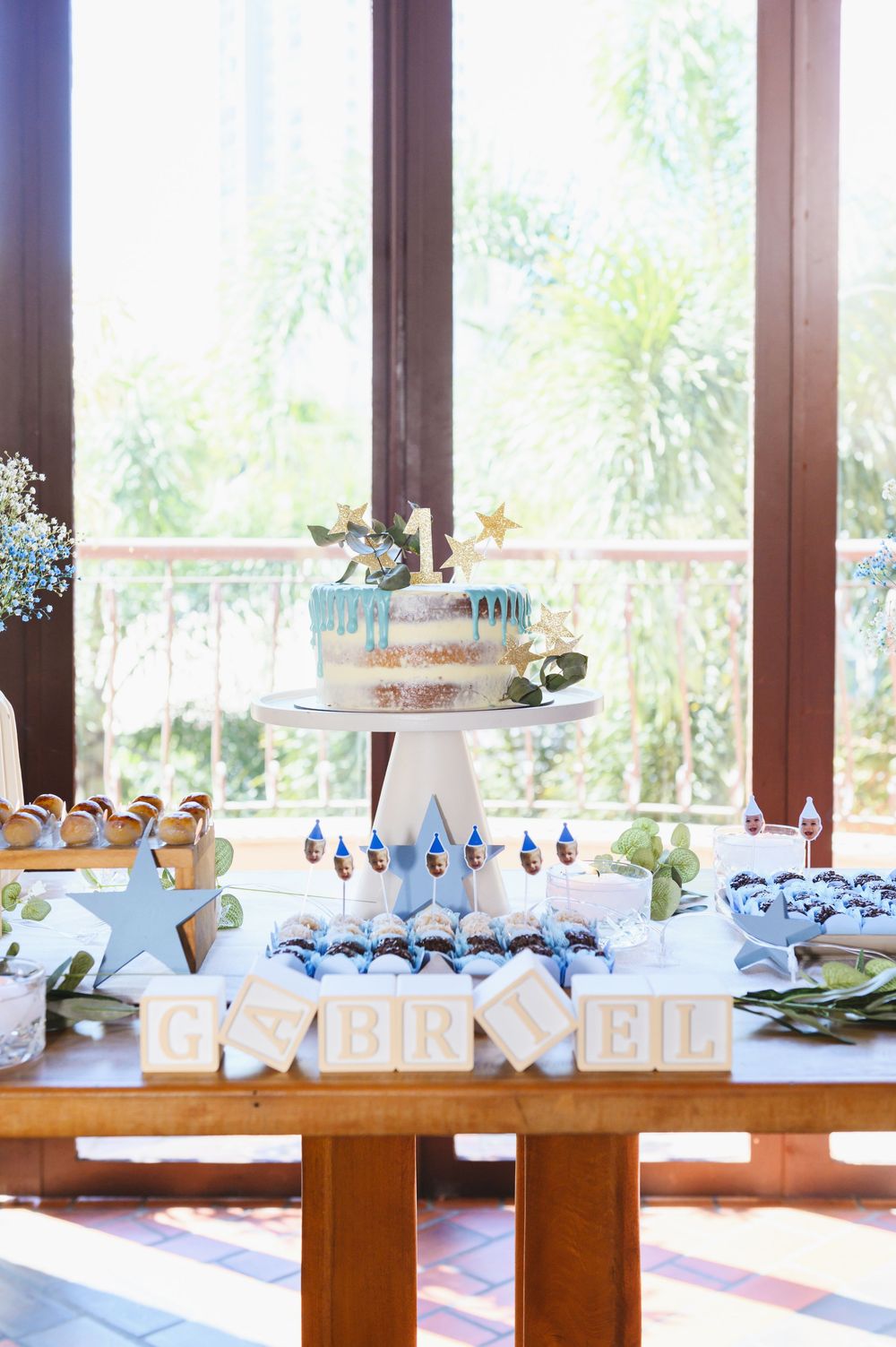 Gabriel's first birthday dessert table with a smash cake on stand, cupcakes, and decorative letter blocks spelling the name.