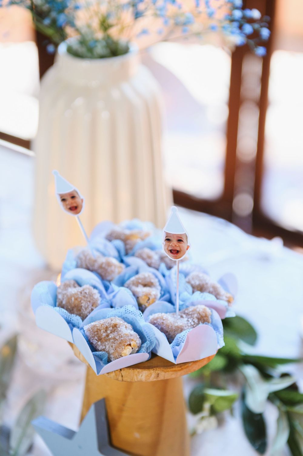 Baby shower donut display in blue cupcake liners with baby face toppers on a wooden stand.