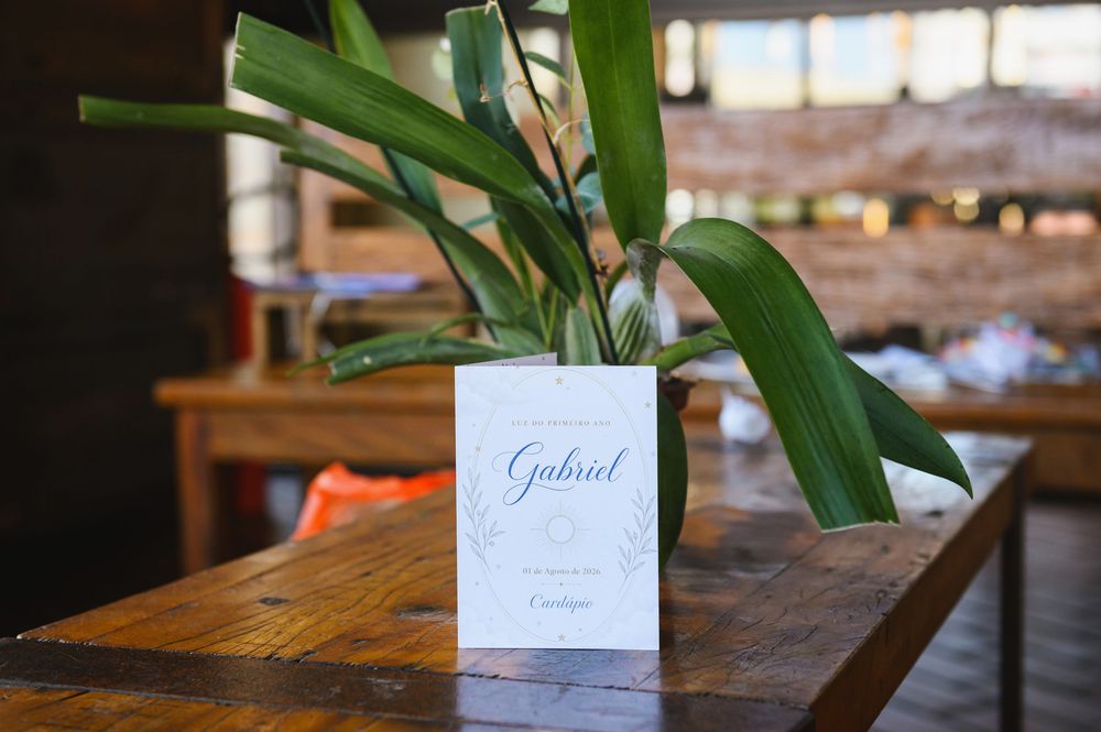 Elegant wedding place card for Gabriel displayed beside tropical green leaves on a rustic wooden table.
