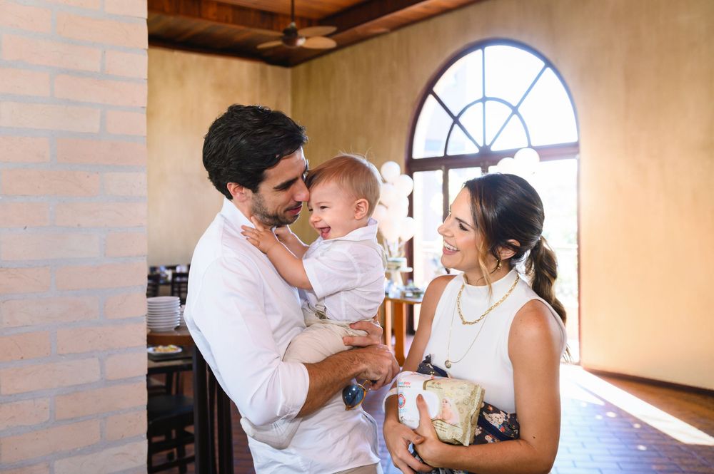 Young couple smiling and holding their baby in a rustic venue with arched windows and warm lighting.