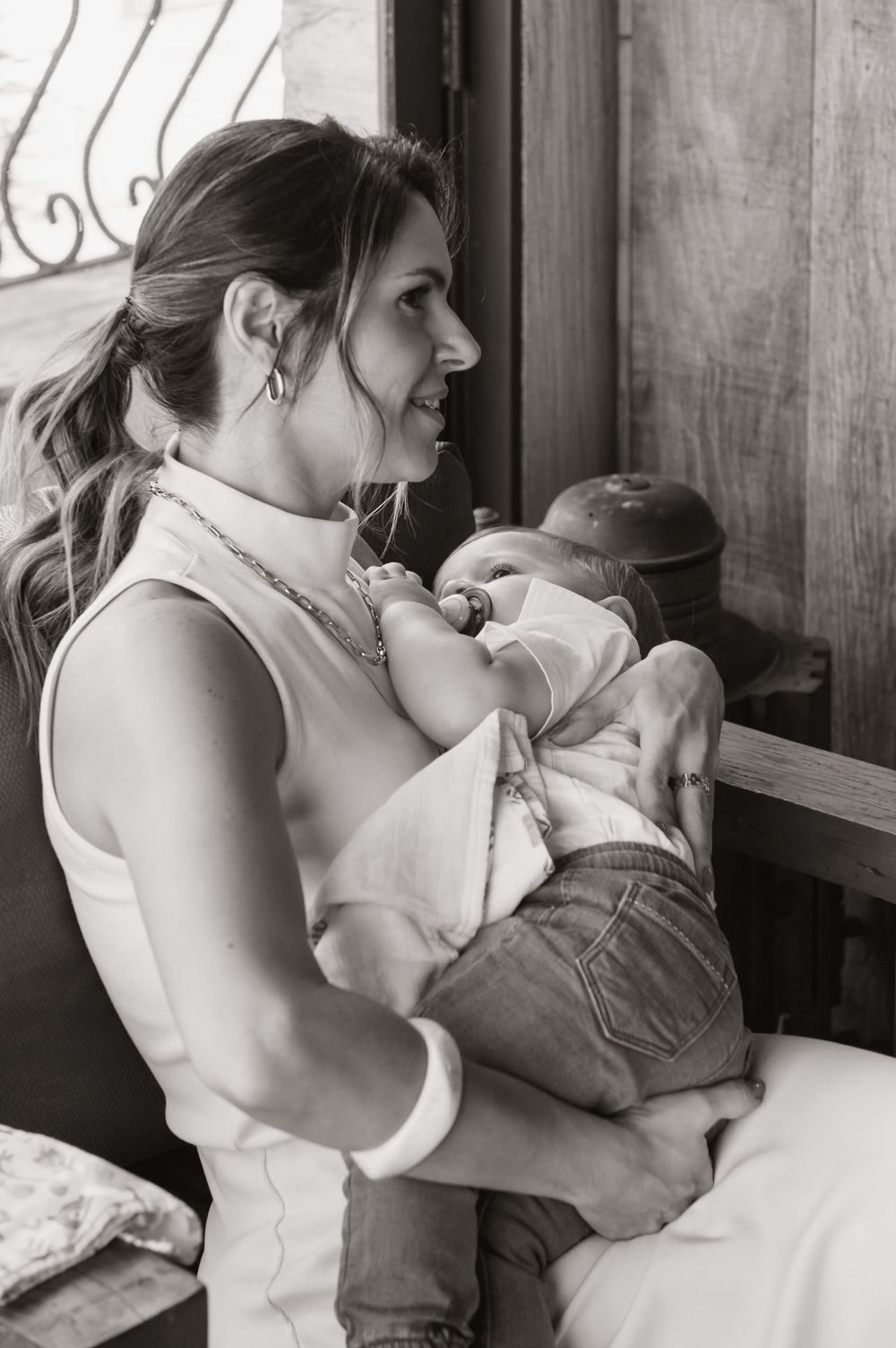 Black and white photo of a mother breastfeeding her newborn baby while sitting near a window indoors.