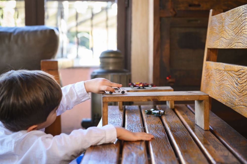Young boy playing with toy cars on a small wooden table indoors.