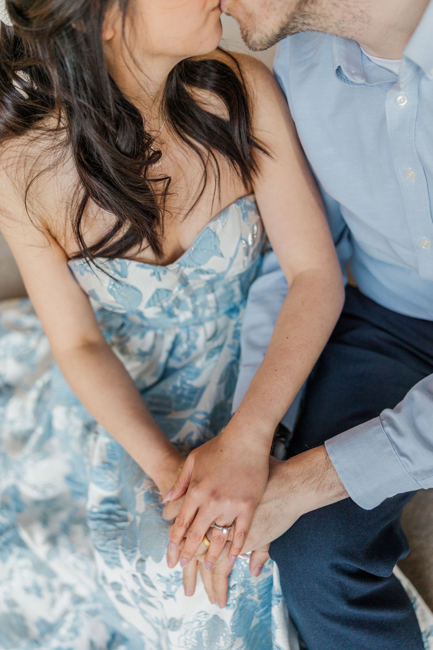 Couple sharing a kiss while displaying an engagement ring, woman wearing a blue floral strapless dress.