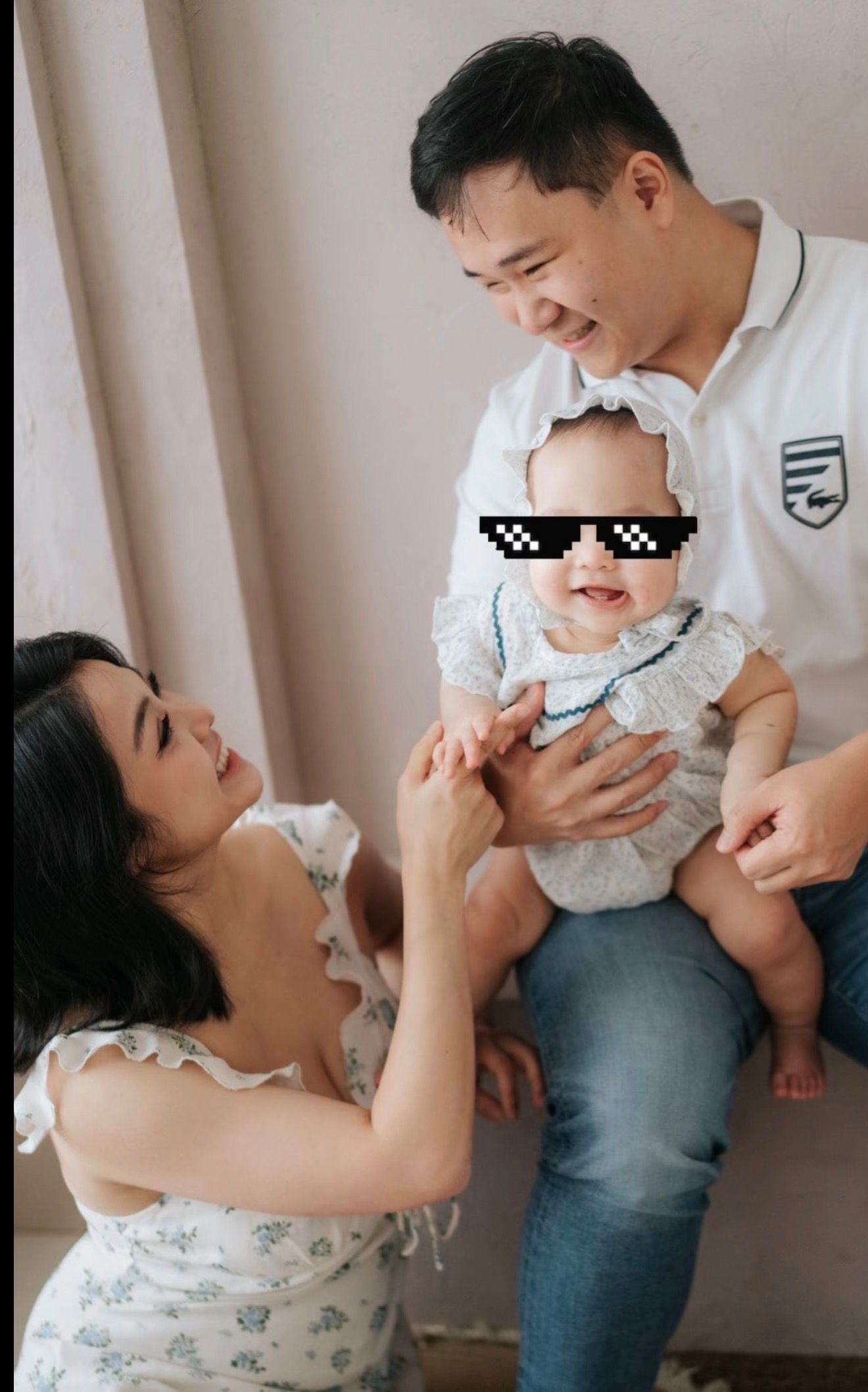 Happy Asian family portrait with parents and baby wearing novelty pixel sunglasses sticker, smiling together indoors.