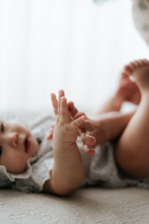 A baby lying on a soft blanket, reaching up with tiny hands and feet in a cozy white onesie.