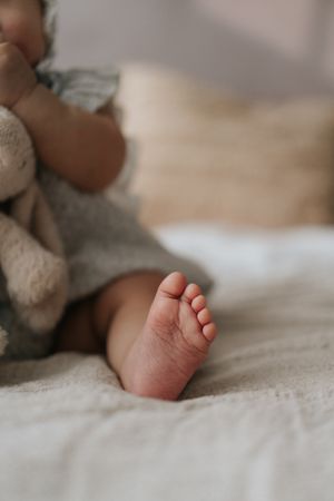 Close-up of a newborn baby's tiny foot resting on a soft white blanket with a stuffed animal in the background.