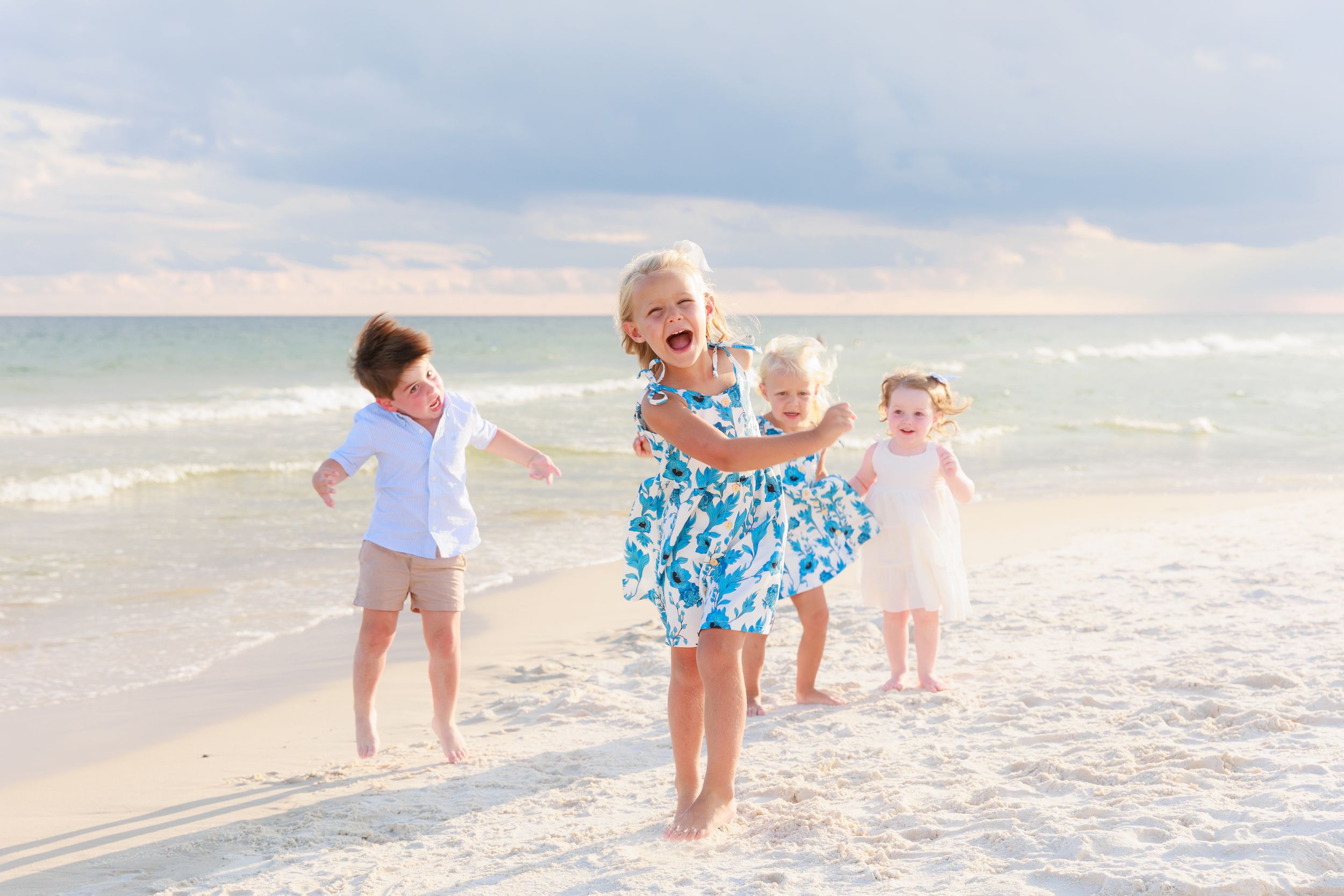 Black and white beach photo of two women playing with three children in sand dunes with sea oats in background.