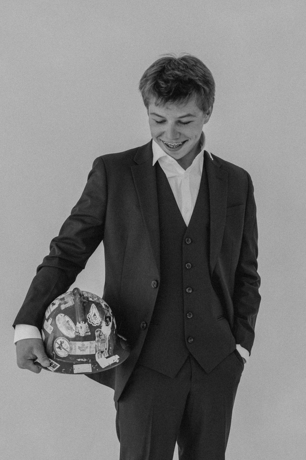 Black and white portrait of a smiling teen boy in a three-piece suit holding a decorated helmet.