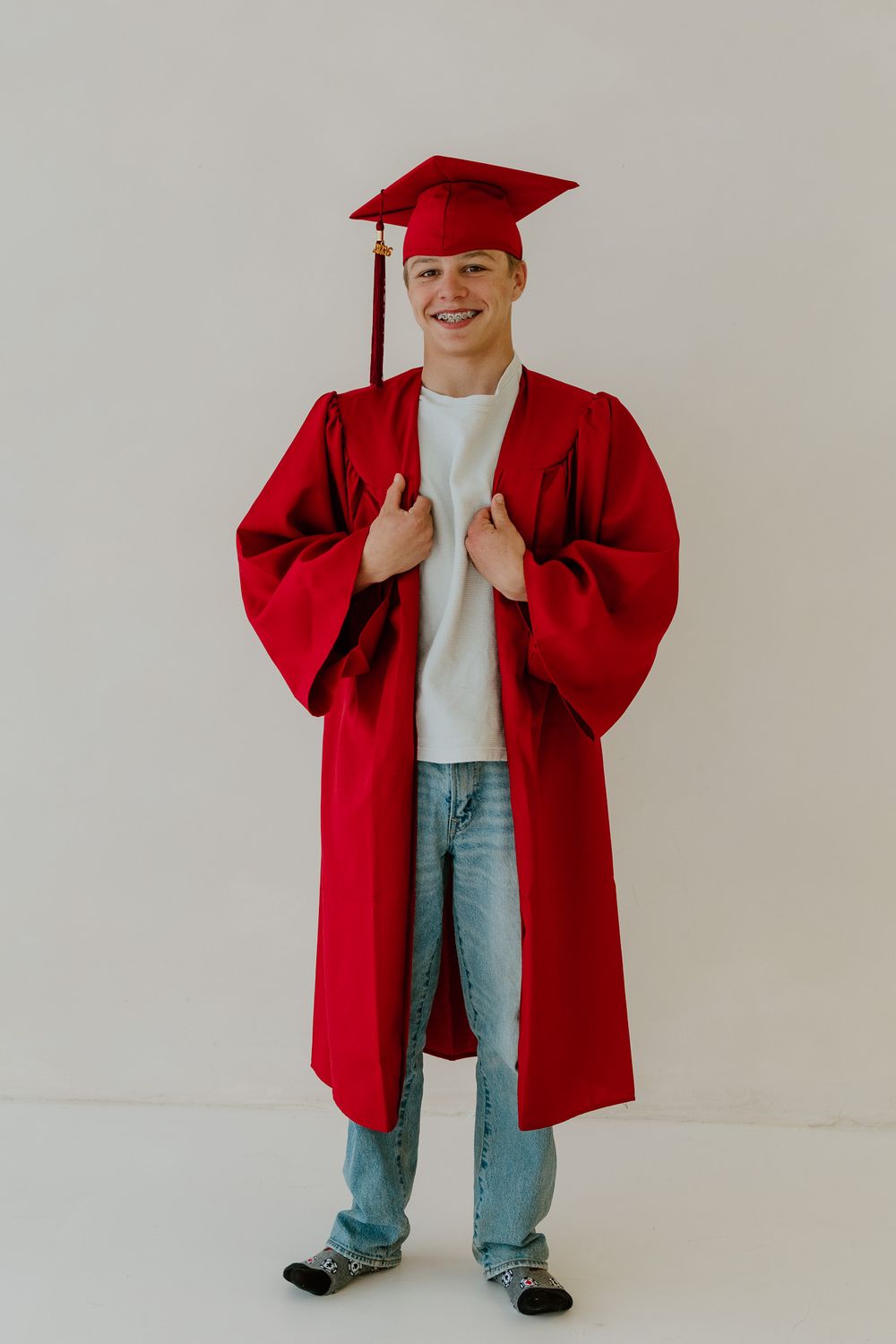 Smiling young man in red graduation cap and gown standing confidently for senior portrait photo.