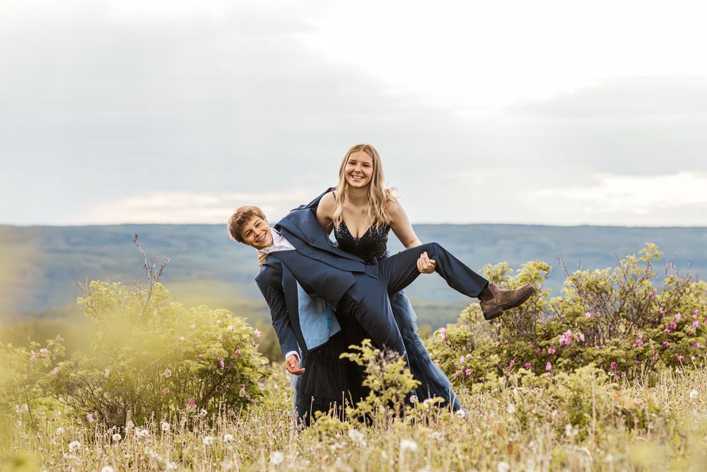 Young man carrying a laughing blonde woman on his back in a scenic overlook meadow.