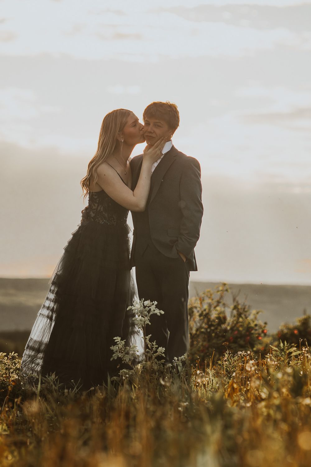 Couple sharing a tender kiss in a sun-drenched field during a golden hour photoshoot.