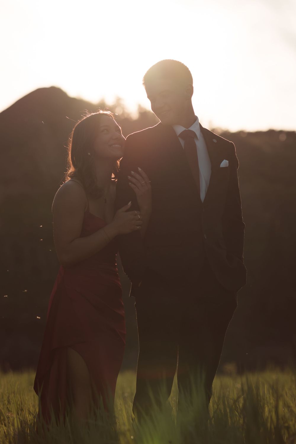 Romantic silhouette of a couple in formal wear standing in a golden sunlit field at dusk.