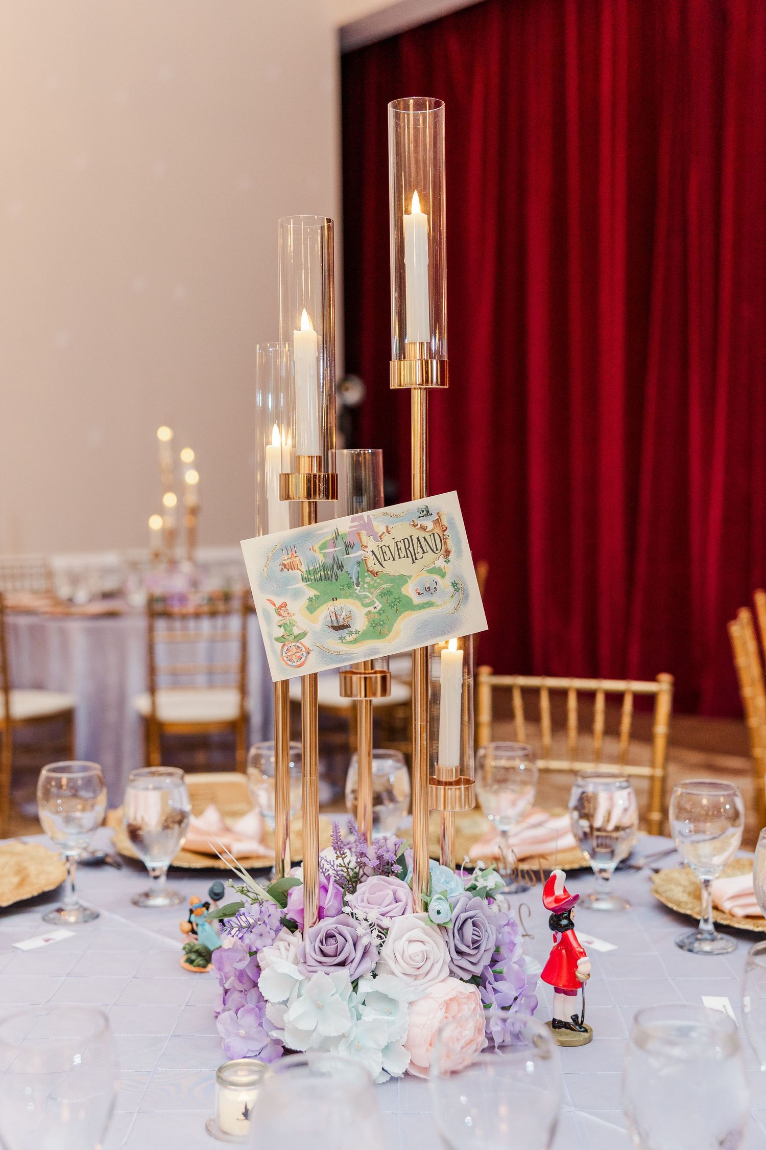 Elegant wedding centerpiece with gold candelabra, purple and white flowers, and a decorative table number card.
