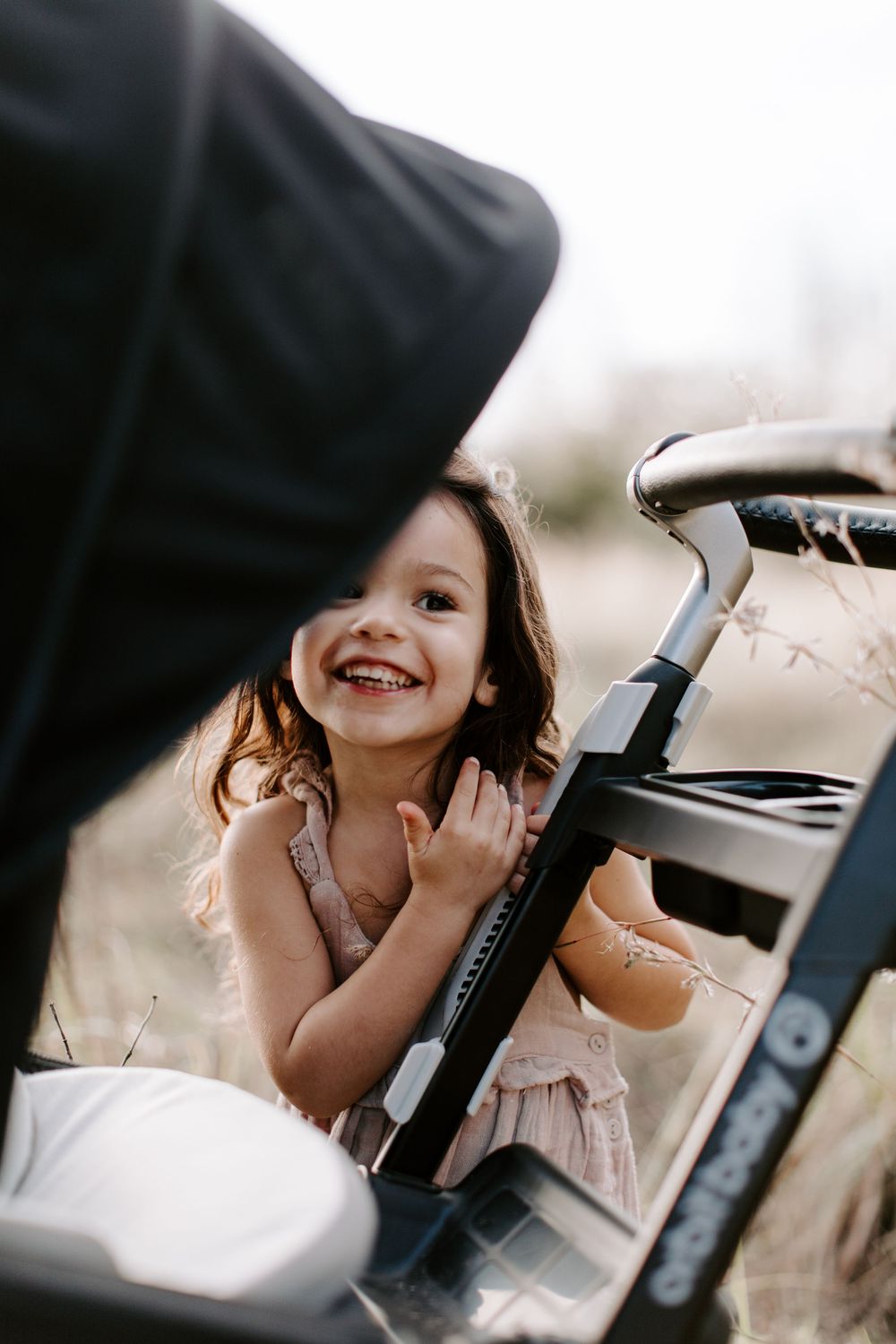 Young child peeks playfully through a car window with a bright smile.