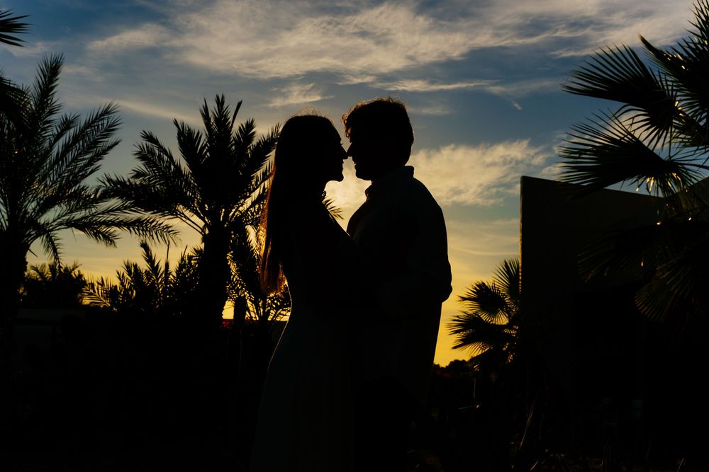Silhouette of a romantic couple nearly kissing at sunset with palm trees and colorful sky in the background.