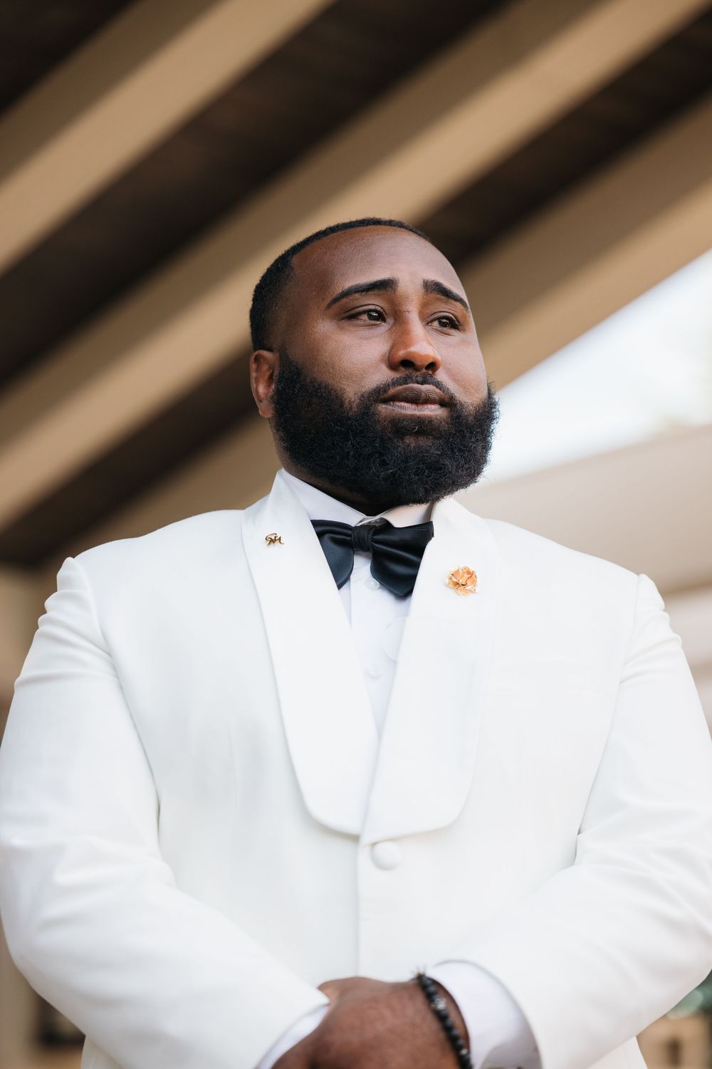 Elegant man in white tuxedo jacket with black bow tie and beard, posing confidently outdoors.
