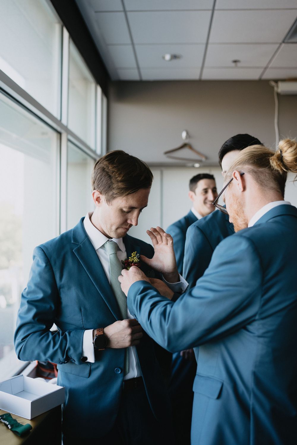 Groomsmen in blue suits pinning a boutonniere on the groom before a wedding ceremony.