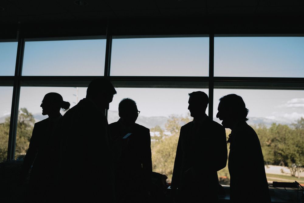 Silhouettes of four people conversing near large windows with a bright outdoor landscape backdrop.